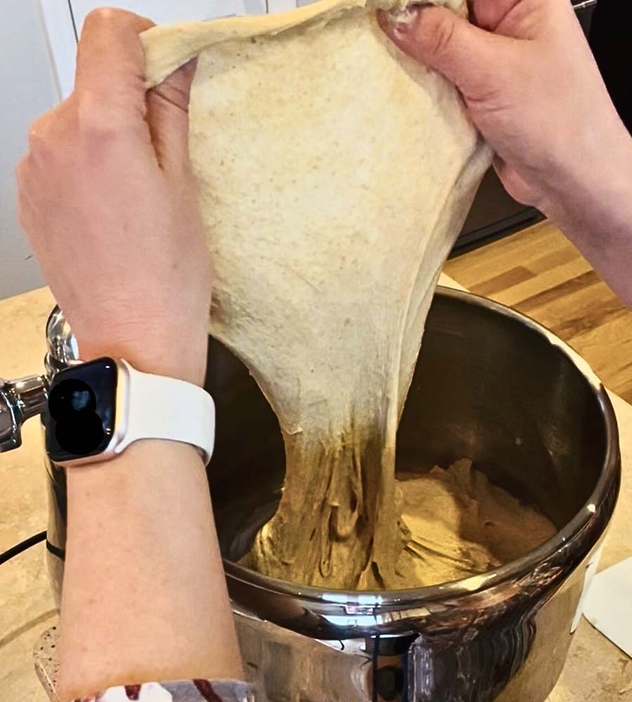 Stretching fresh milled flour dough to show windowpane gluten development in a mixer bowl.