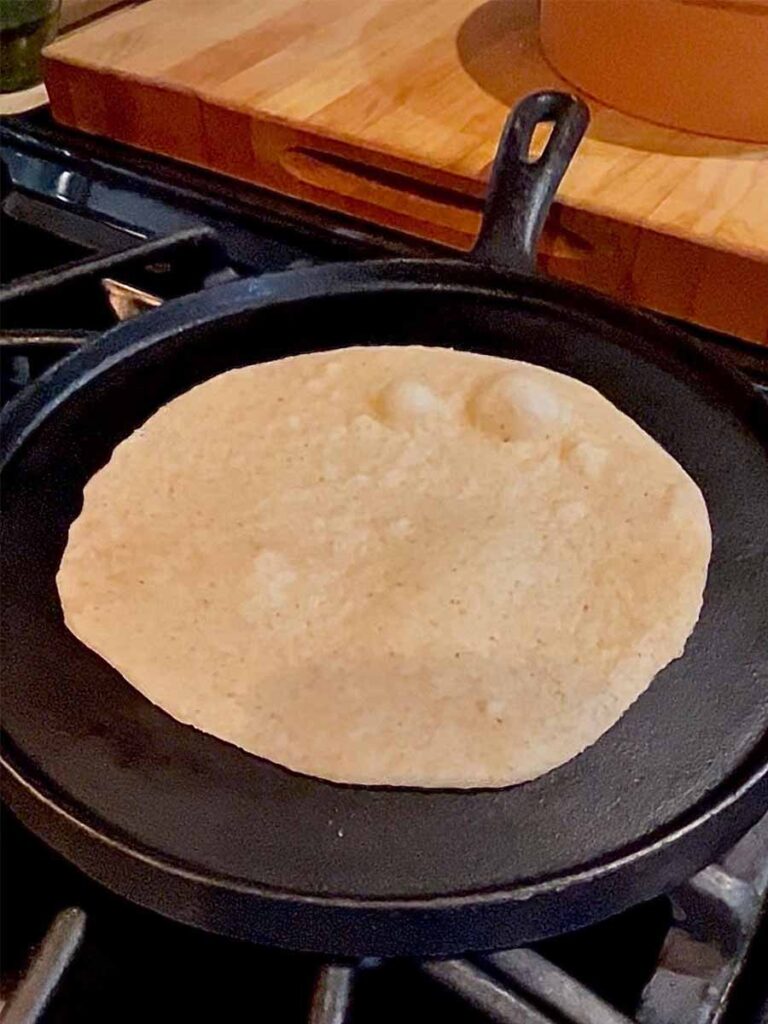 fresh milled flour tortilla cooking in skillet with bubbles forming on the surface