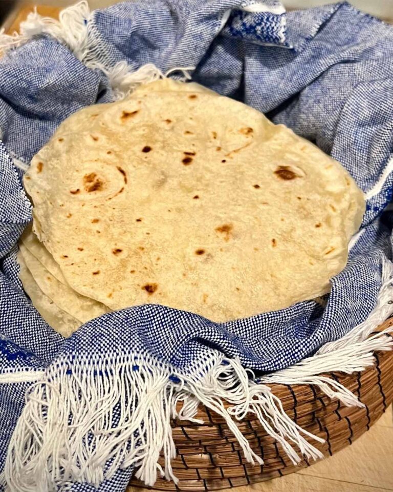 Fresh milled flour tortillas stacked in a basket with a blue towel
