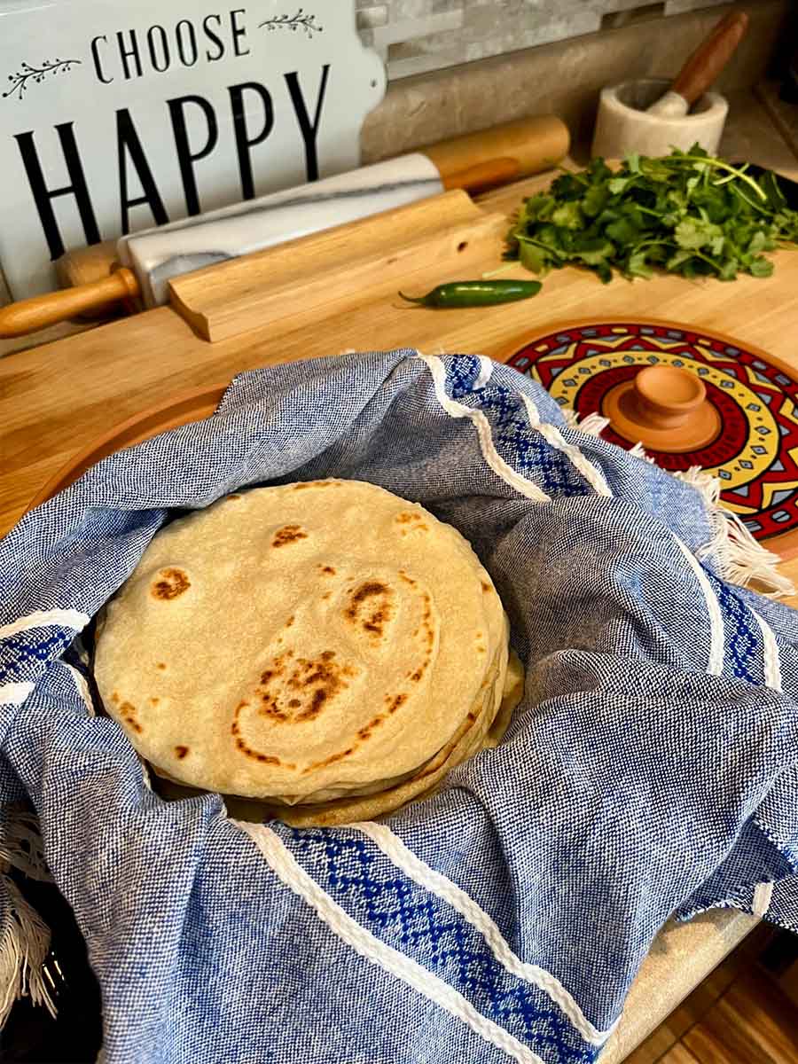 Soft fresh milled flour tortillas stacked in a basket lined with a blue cloth